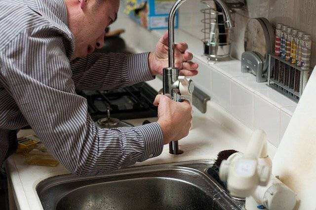 Airbnb Hosting A man performing maintenance on a kitchen sink in an Airbnb rental.